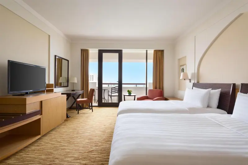 Chambre lumineuse avec deux lits et balcon donnant sur la mer.