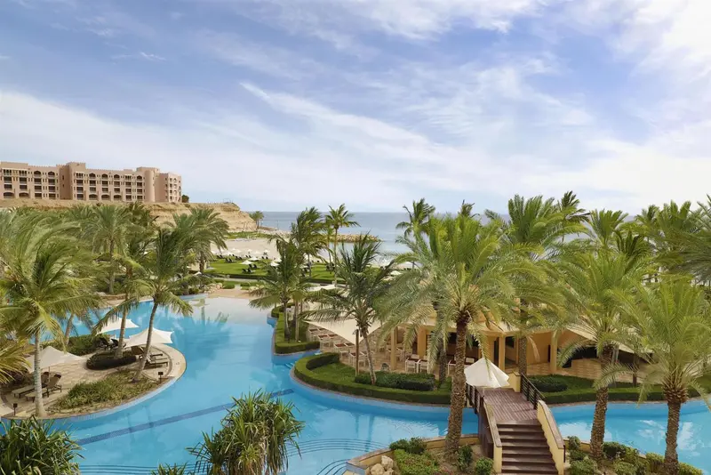 Vue aérienne d'un complexe hôtelier avec piscine sinueuse et végétation luxuriante.
