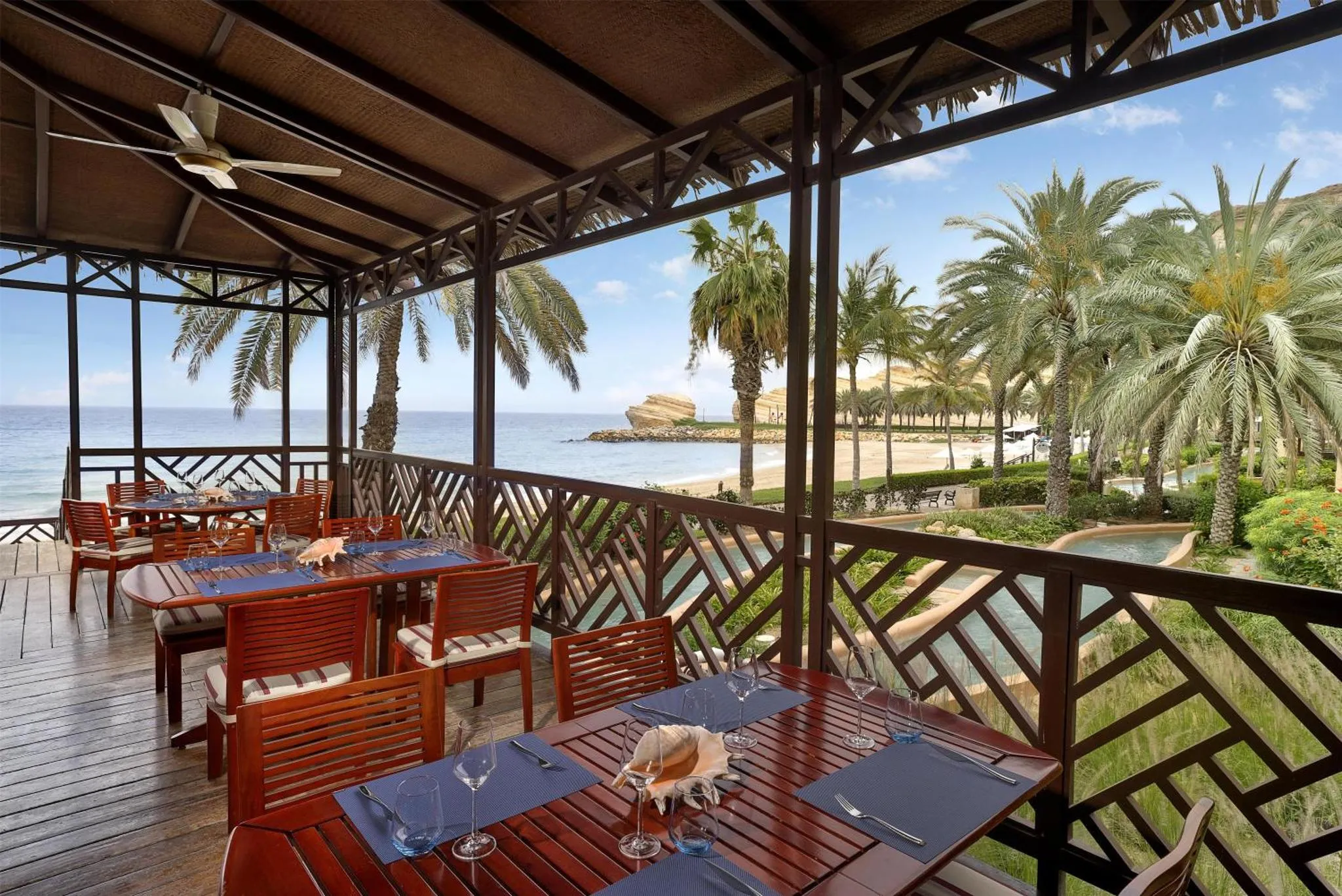 Terrasse ombragée avec tables dressées face à la mer et à la végétation.