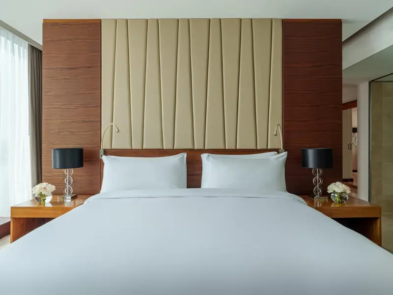 Une chambre avec un grand lit recouvert de draps blancs et une tête de lit en bois et tissu.