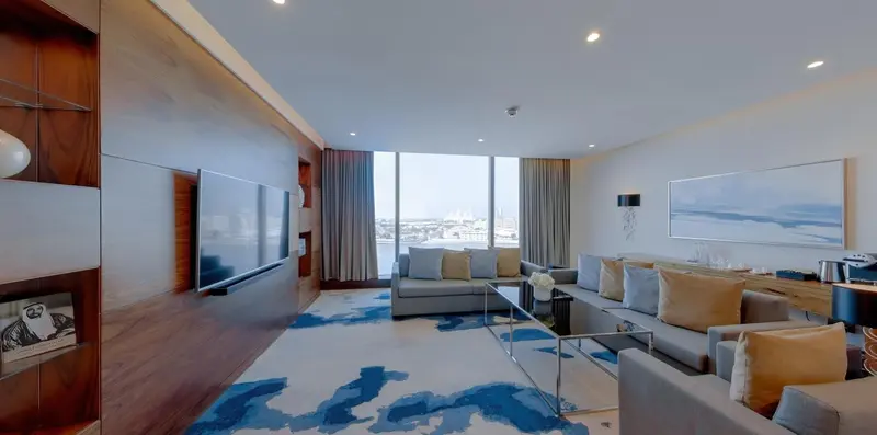 Un salon spacieux avec un grand canapé et une télévision murale face à une baie vitrée.