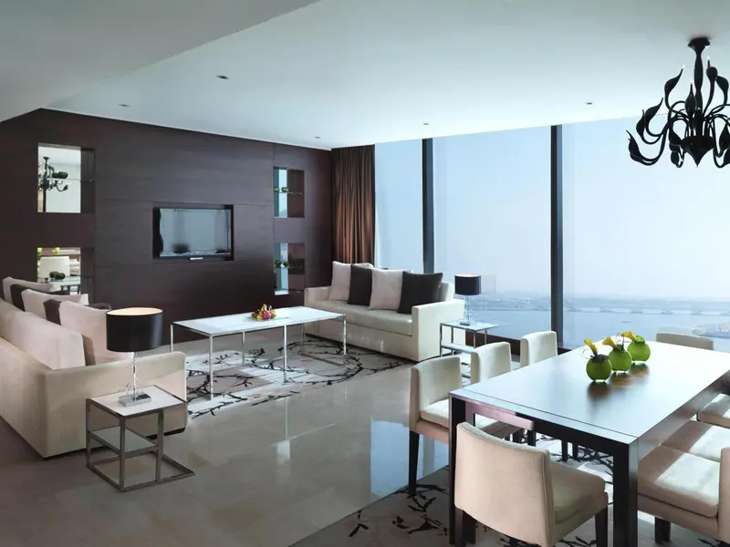 Un salon moderne avec canapés clairs et une table basse, donnant sur une vue urbaine.