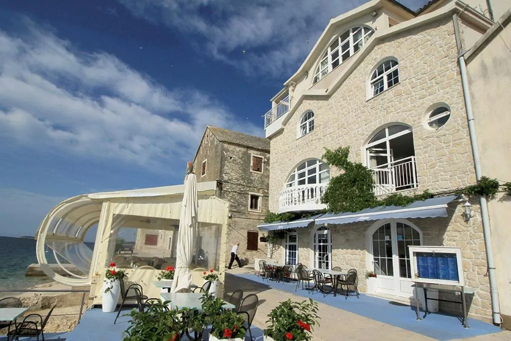 Bâtiment en pierre claire avec des ouvertures cintrées et une terrasse ombragée en bord de mer.