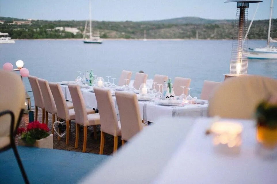 Une longue table est dressée pour un repas en extérieur, face à la mer.