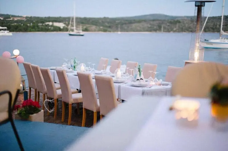 Une longue table est dressée pour un repas en extérieur, face à la mer.