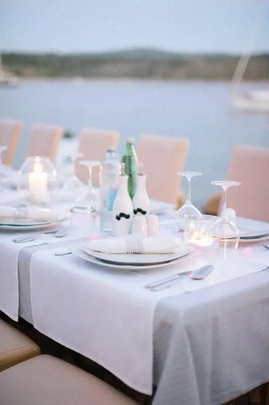 Une table est dressée pour un repas en extérieur avec des verres, des assiettes et des couverts.