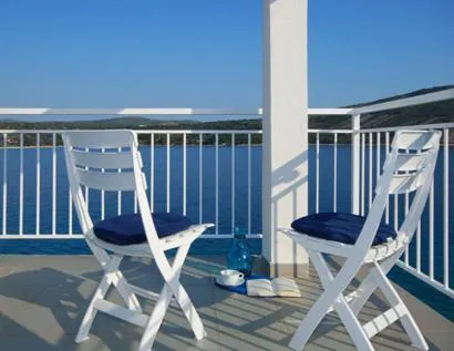 Deux chaises blanches avec coussins bleus sont placées sur une terrasse ensoleillée avec vue sur la mer.