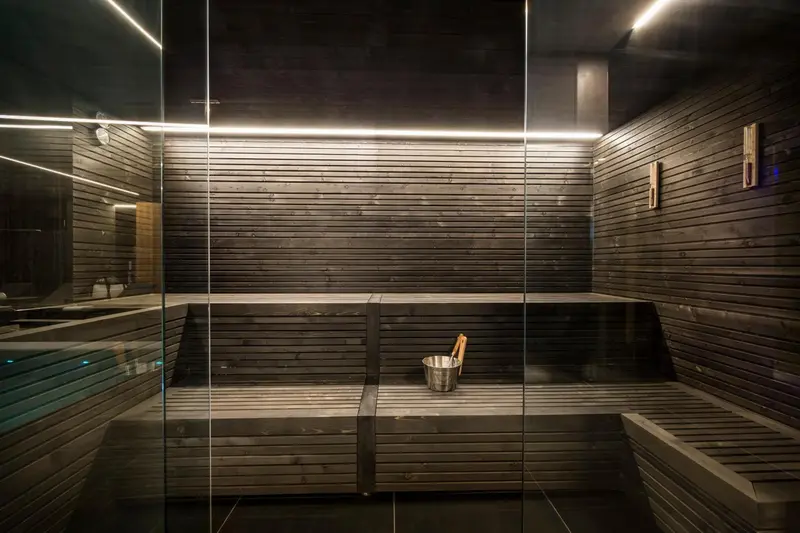 Intérieur d'un sauna en bois sombre éclairé par des bandes lumineuses.