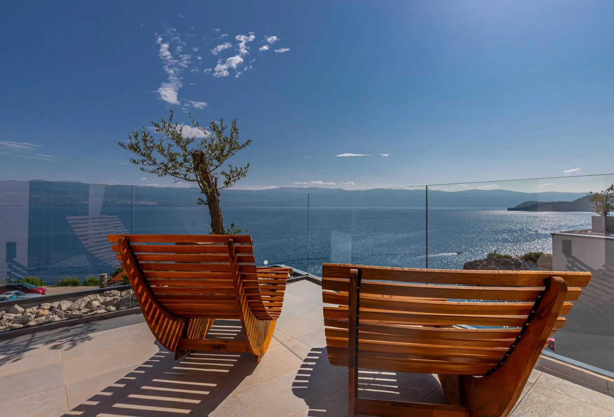 Deux chaises longues en bois sur une terrasse ensoleillée avec vue sur la mer.