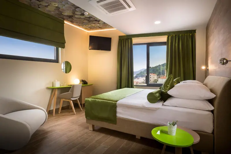 Chambre lumineuse avec un lit recouvert d'une courtepointe verte et une vue sur un paysage vallonné.