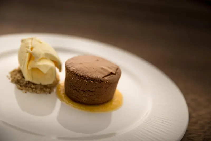 Un dessert au chocolat avec une boule de glace vanille est présenté sur une assiette blanche.