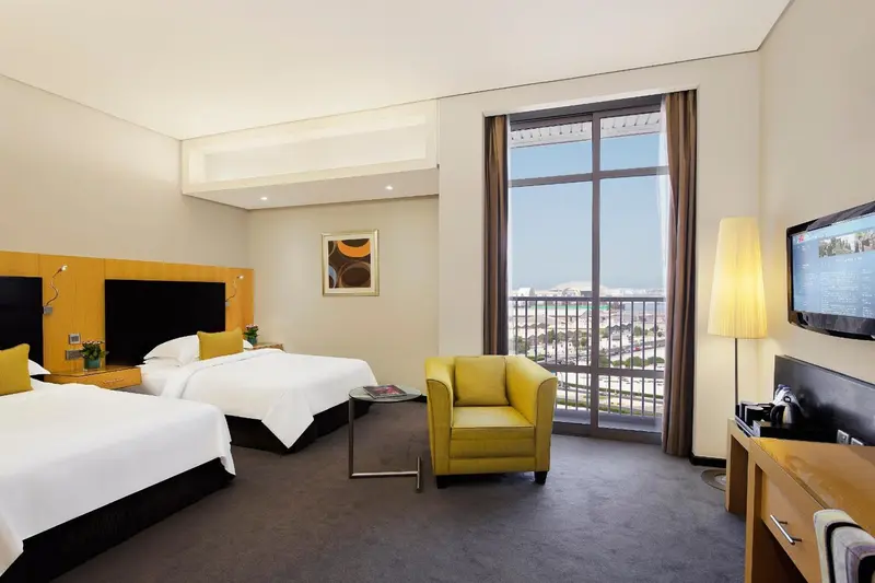 Une chambre lumineuse avec deux lits et un fauteuil jaune.