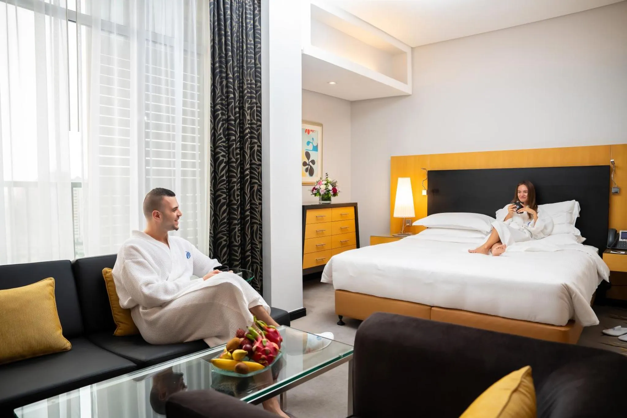 Un couple se détend dans un salon de chambre d'hôtel avec un plateau de fruits.