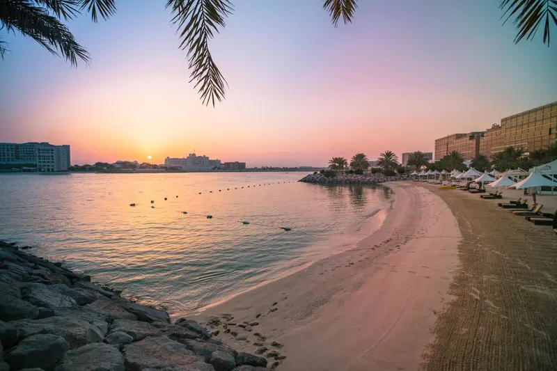 Plage de sable fin bordée d'une eau calme au coucher du soleil.