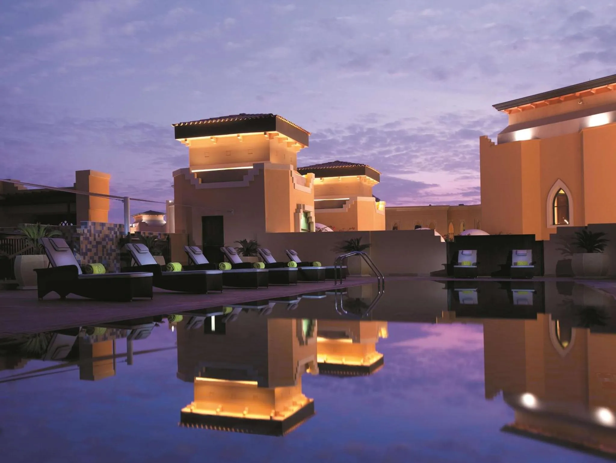 Piscine illuminée au crépuscule avec transats et architecture beige.