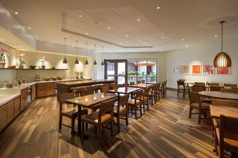 Une salle lumineuse avec des tables et des chaises en bois, un buffet de petit-déjeuner et des suspensions décoratives.