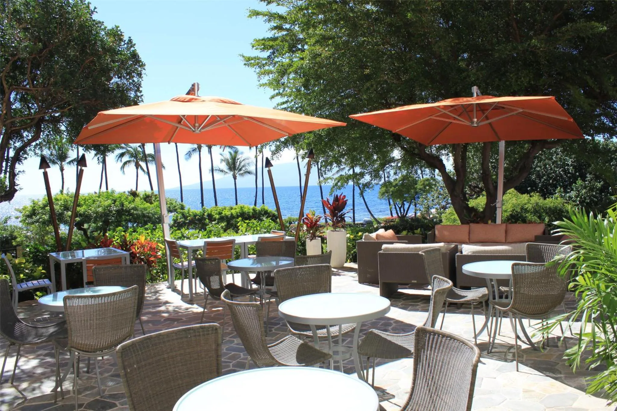 Terrasse ombragée avec tables et chaises donnant sur la mer.