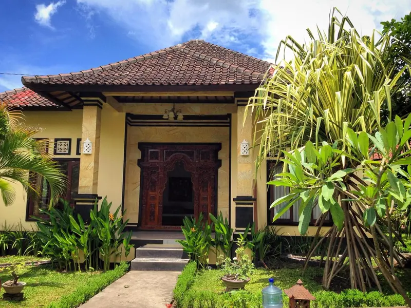 Façade d'une maison jaune à toit de tuiles, entourée de végétation tropicale.