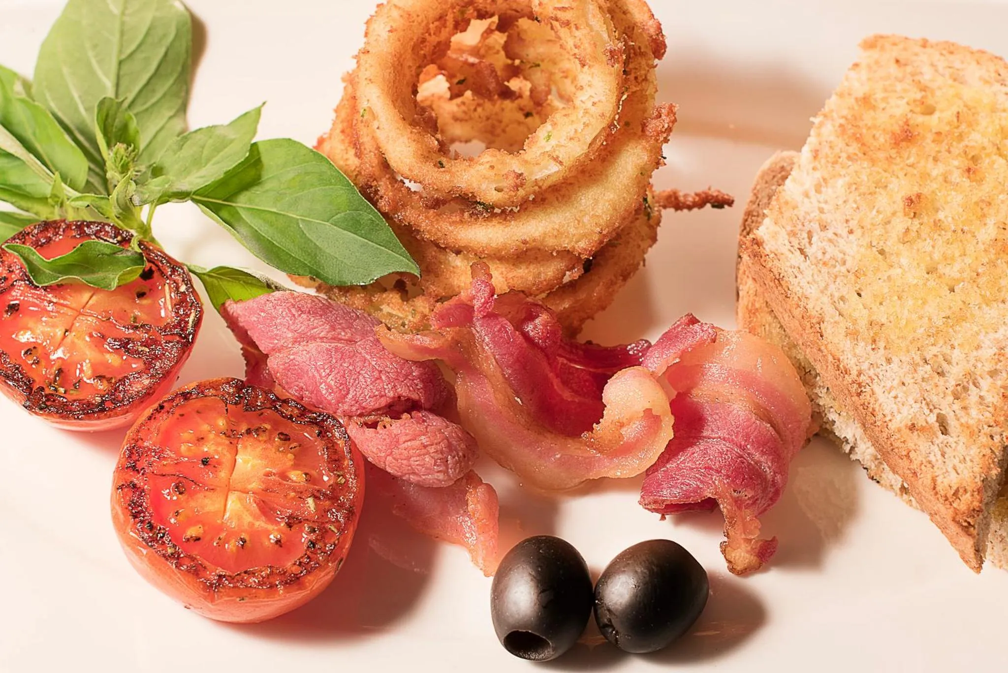 Assiette de nourriture avec des rondelles d'oignon frites, du bacon, des tomates et du pain grillé.