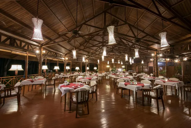 Une salle à manger extérieure avec des tables dressées et des luminaires suspendus.