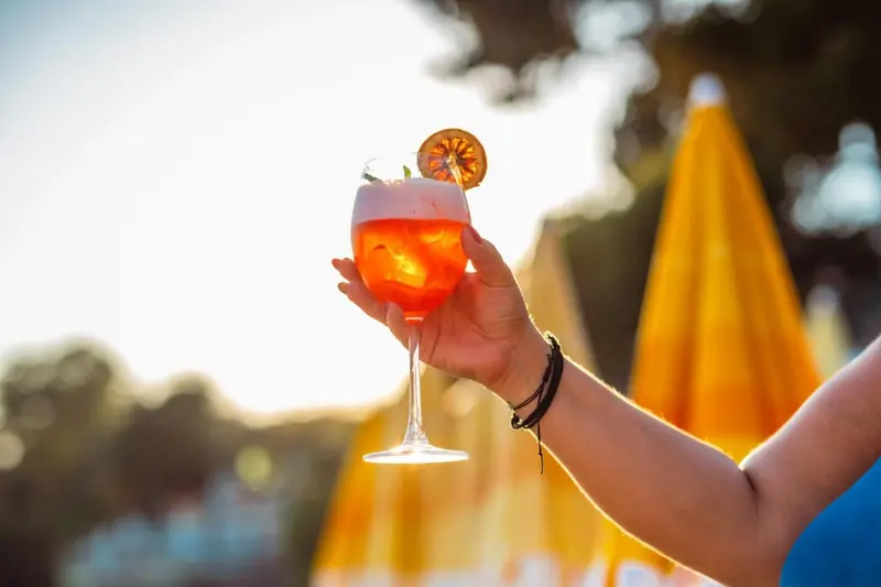 Une main tenant un cocktail coloré sur fond flou de parasols.