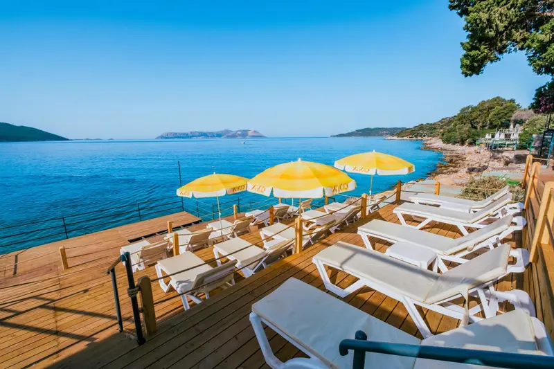 Terrasse en bois avec transats et parasols jaunes face à la mer.