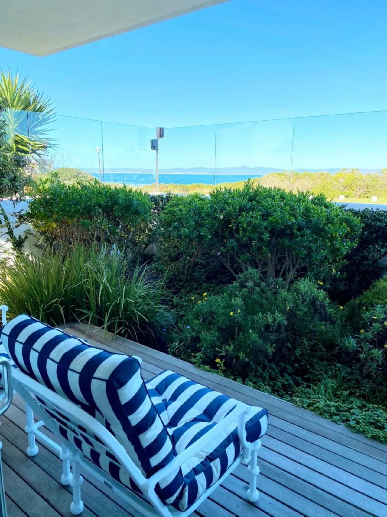 Transat rayé sur une terrasse en bois avec vue sur la mer et la végétation.