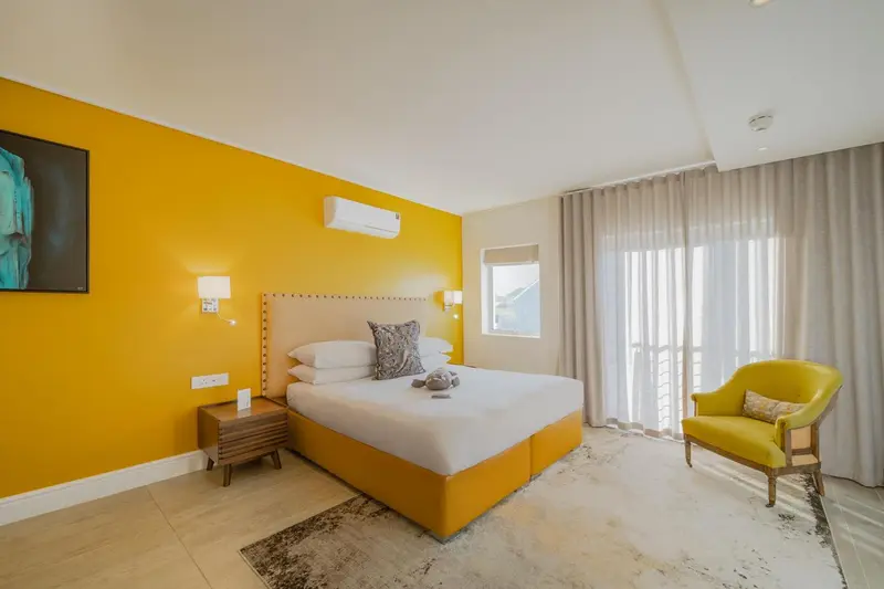 Une chambre lumineuse avec un grand lit et un fauteuil jaune.