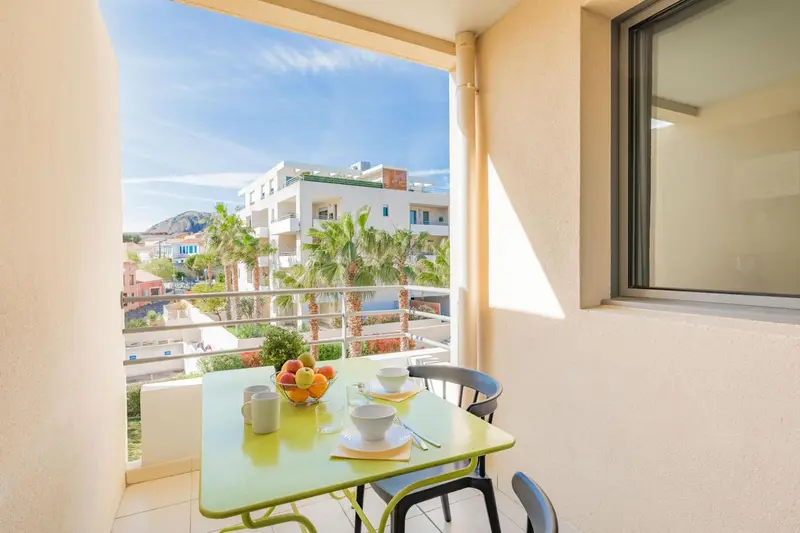 Une table verte est mise en scène sur une terrasse ensoleillée avec vue sur des bâtiments et des palmiers.