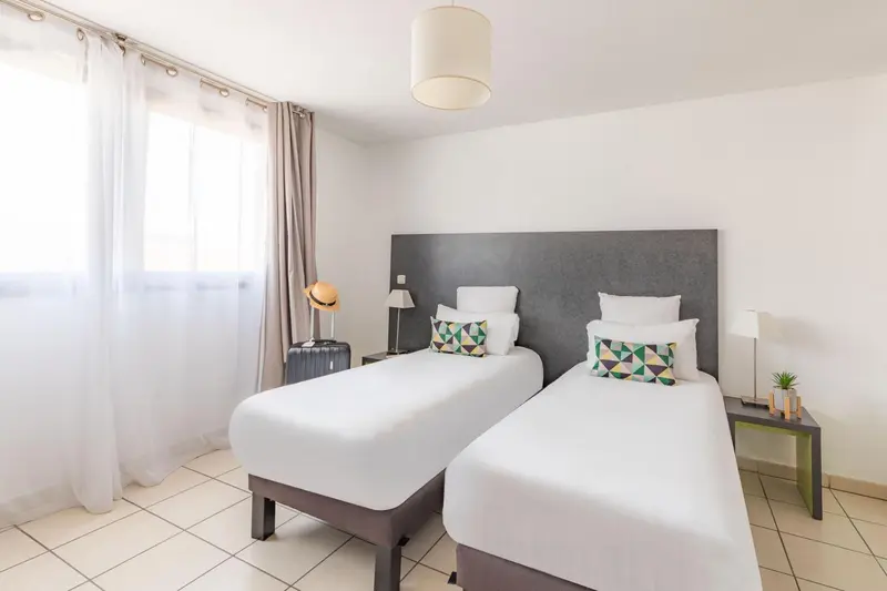 Une chambre lumineuse avec deux lits simples et une décoration sobre.