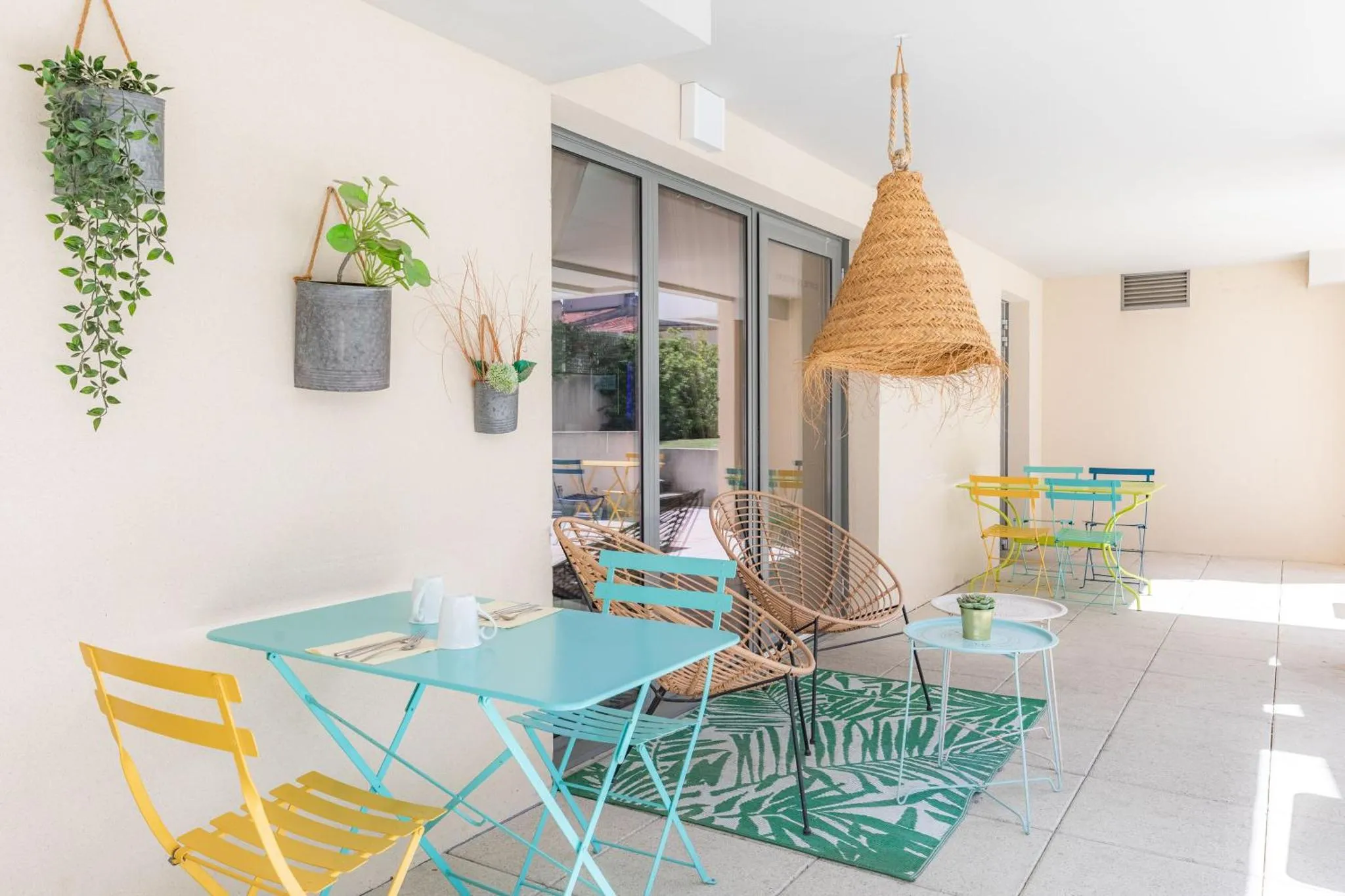 Terrasse ombragée avec tables et chaises colorées.