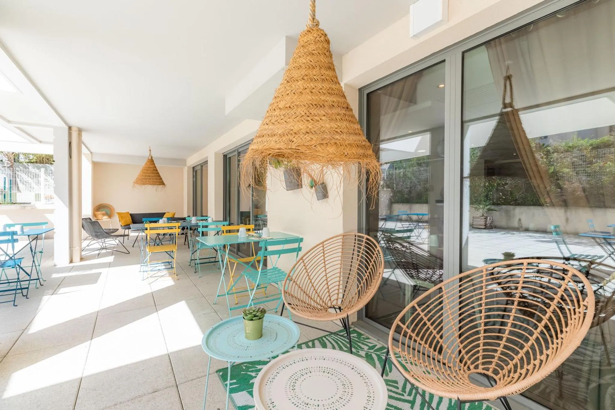 Terrasse ombragée avec tables et chaises colorées.