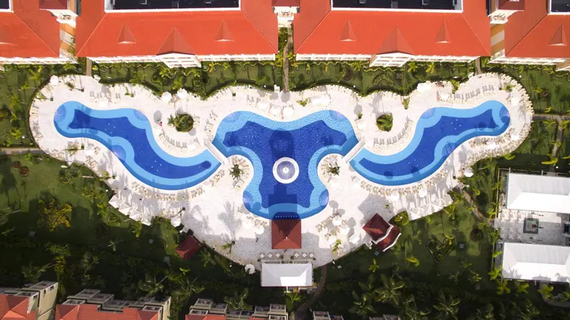 Vue aérienne d'une piscine sinueuse bordée de transats et de palmiers.