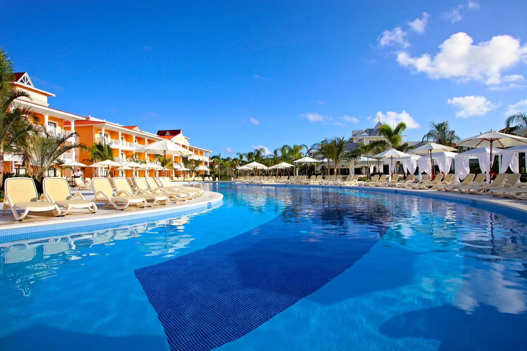 Transats alignés au bord d'une piscine turquoise sous un ciel bleu nuageux.
