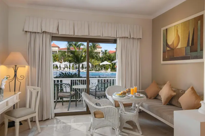 Une chambre lumineuse s'ouvre sur une terrasse avec vue sur une piscine et la végétation.