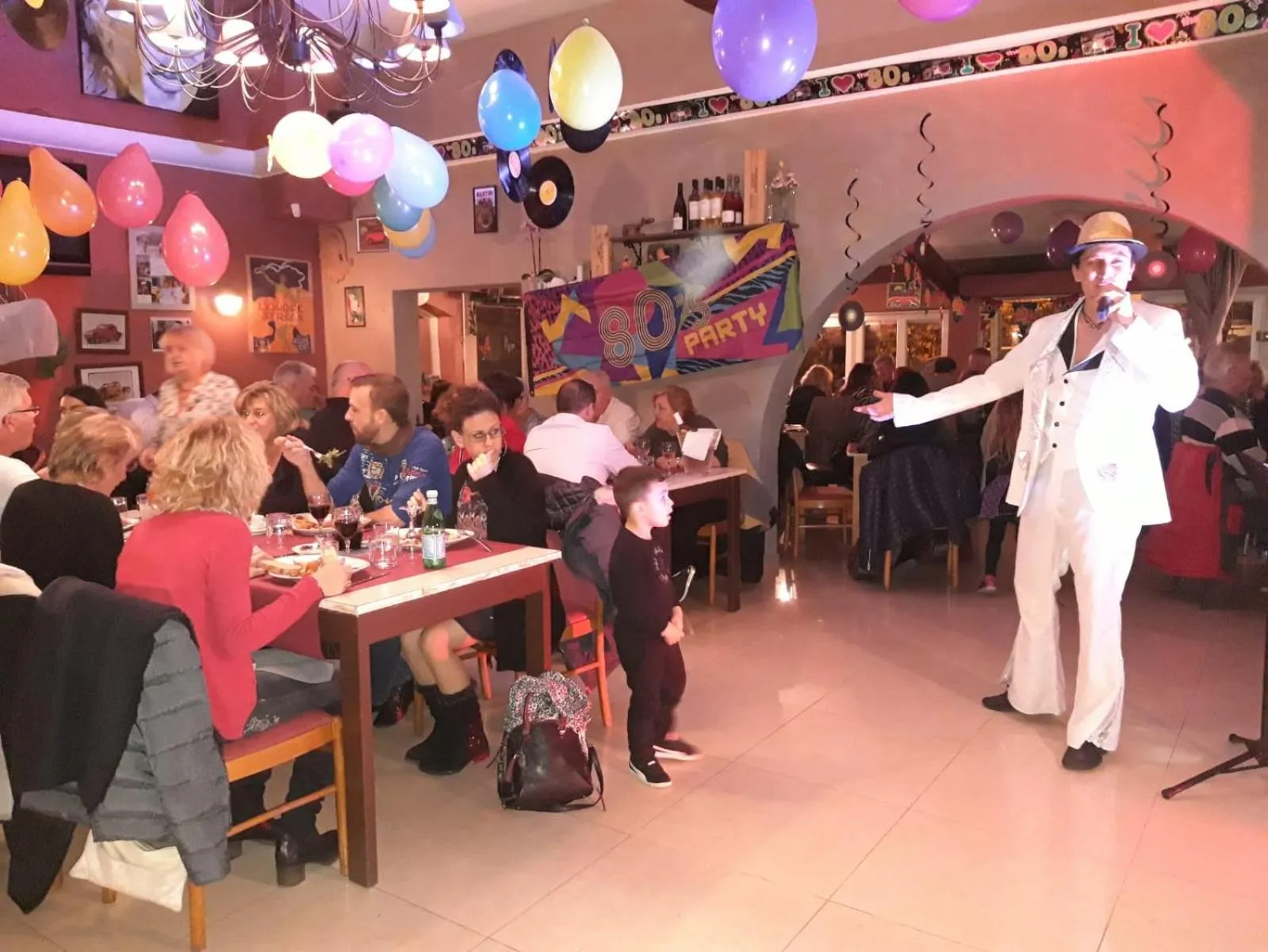 Une salle de restaurant animée avec des convives et un artiste sur scène.