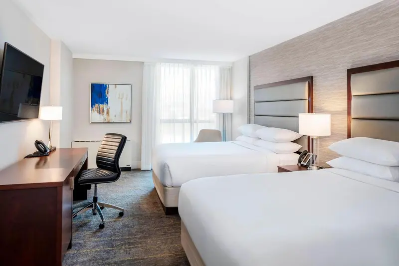 Une chambre d'hôtel avec deux lits et un bureau près d'une fenêtre.