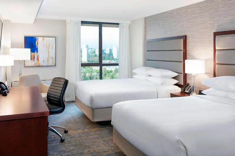 Chambre d'hôtel avec deux lits et bureau près d'une fenêtre.