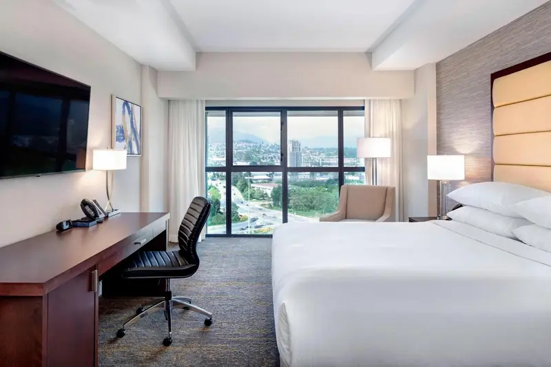 Chambre lumineuse avec bureau, fauteuil et vue sur la ville.