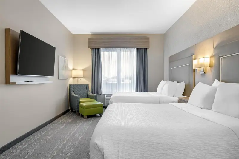 Chambre d'hôtel avec deux lits et un fauteuil vert.