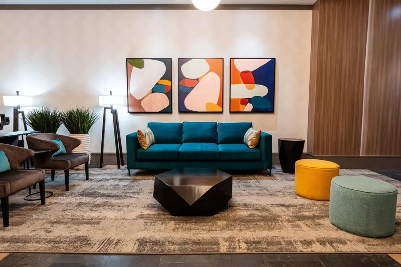 Un canapé turquoise et des fauteuils sont disposés autour d'une table basse dans un espace décoré de tableaux abstraits.