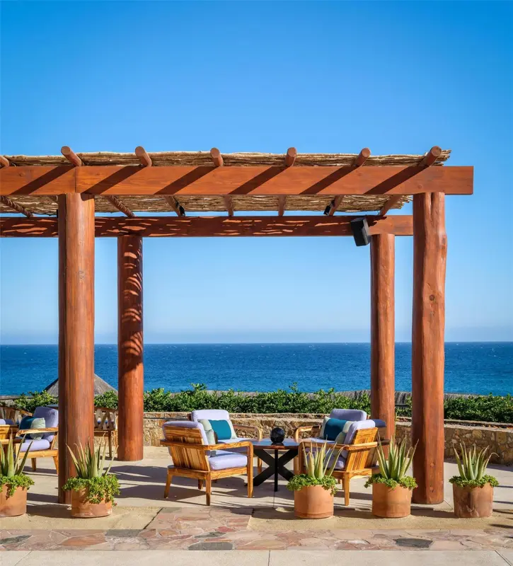 Pergola en bois surplombant une terrasse avec des fauteuils et une vue sur la mer.