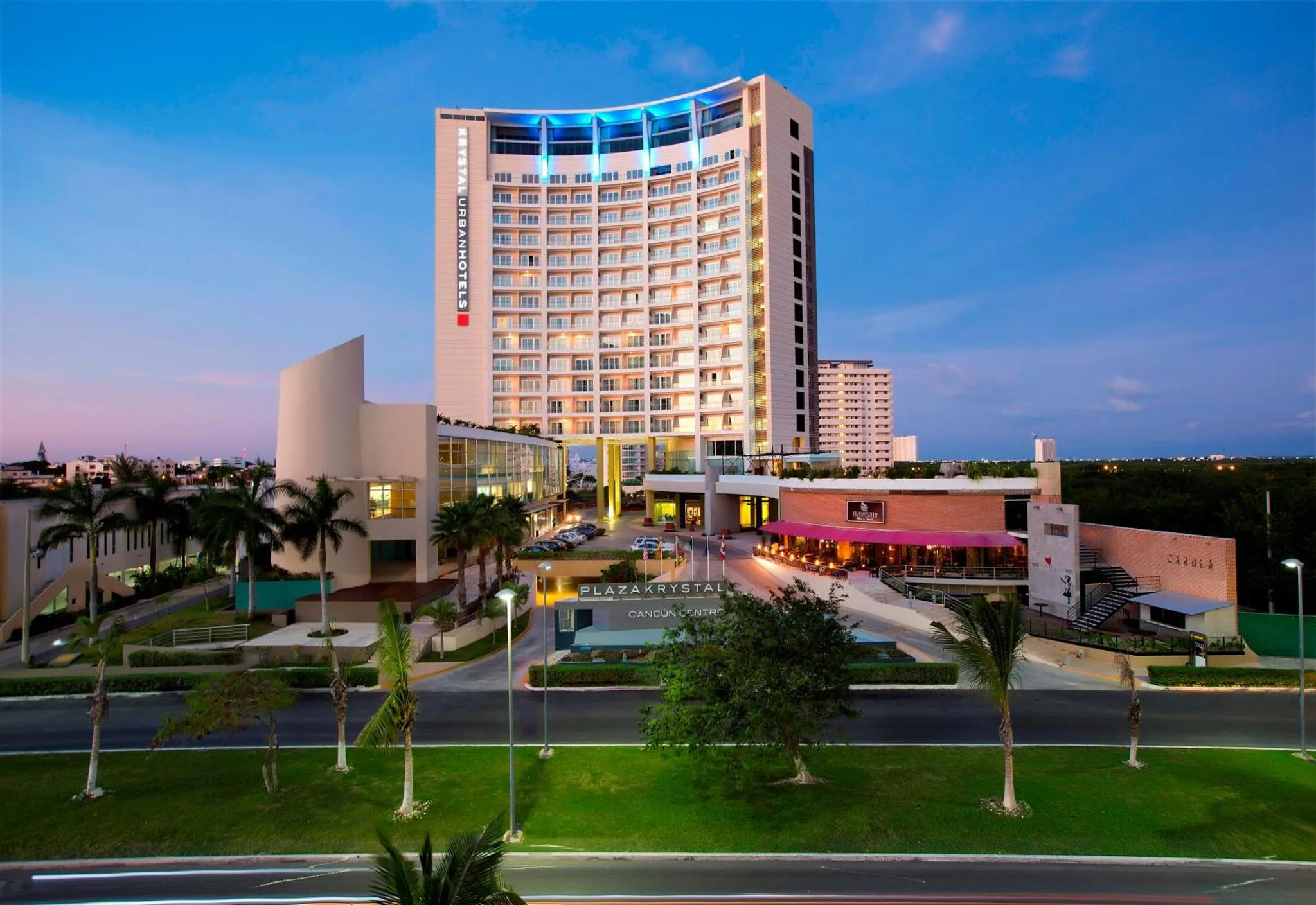 Bâtiment moderne illuminé au crépuscule avec végétation tropicale.