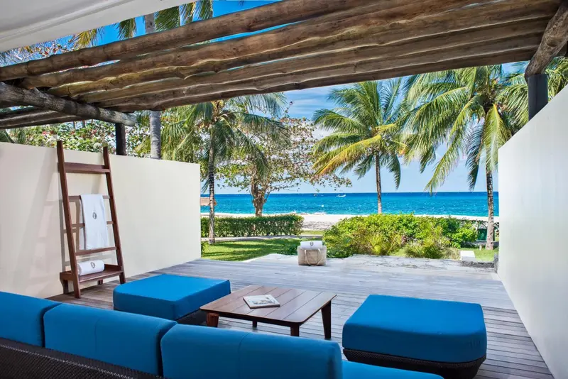 Terrasse aménagée avec canapés bleus donnant sur une plage de sable blanc et la mer.