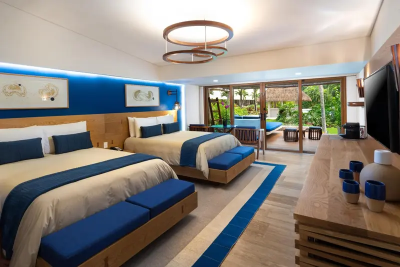 Chambre lumineuse avec deux lits et vue sur une végétation luxuriante.