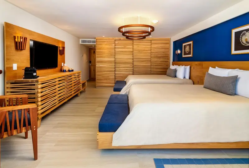 Une chambre lumineuse avec deux lits et un meuble bas en bois.
