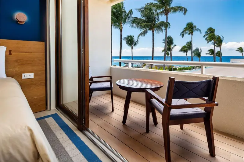 Une terrasse avec deux fauteuils et une petite table offre une vue sur la mer et la végétation.