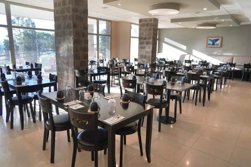 Une salle de restaurant lumineuse avec des tables dressées et des chaises en bois.