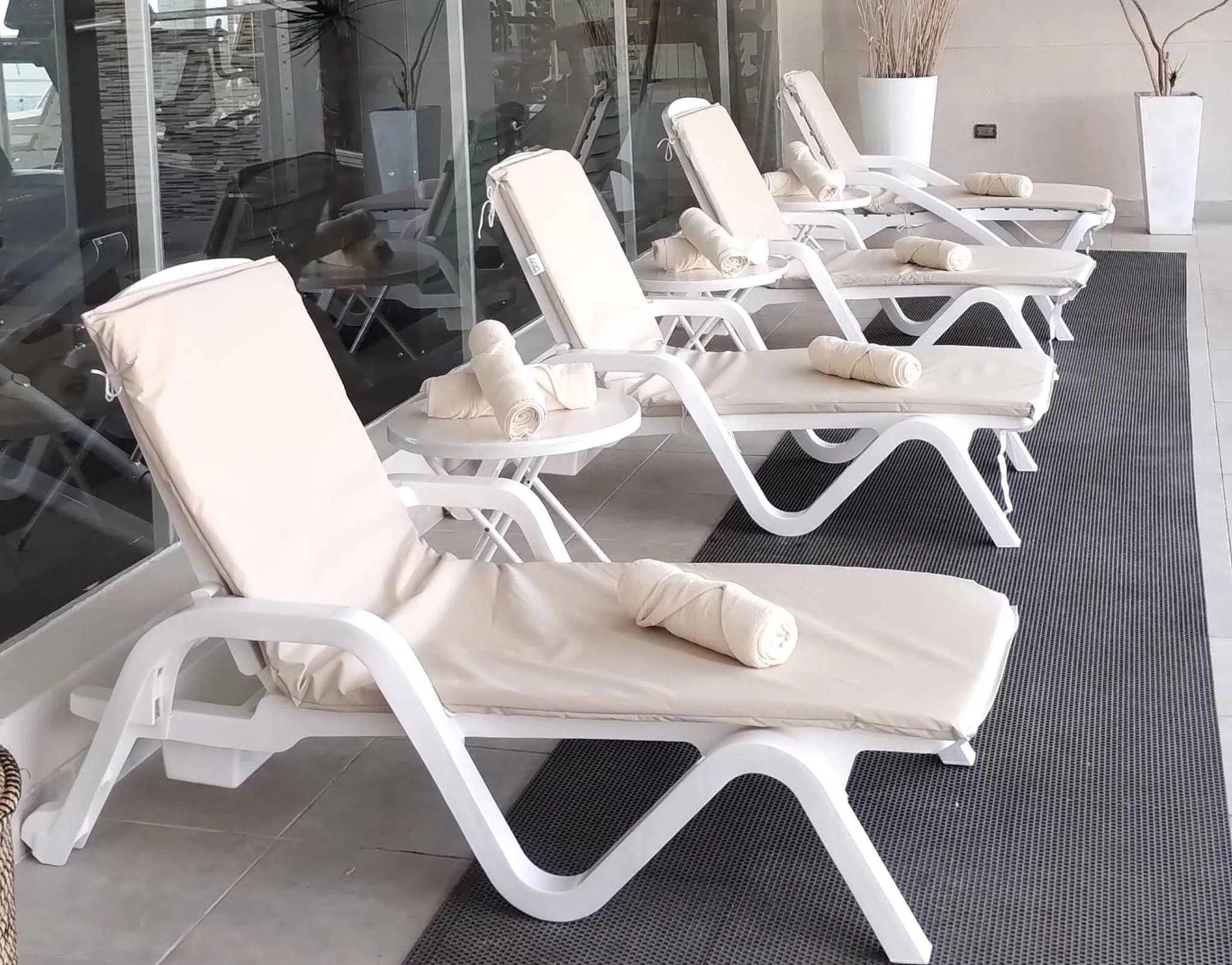 Transats blancs avec serviettes enroulées sur une terrasse carrelée.