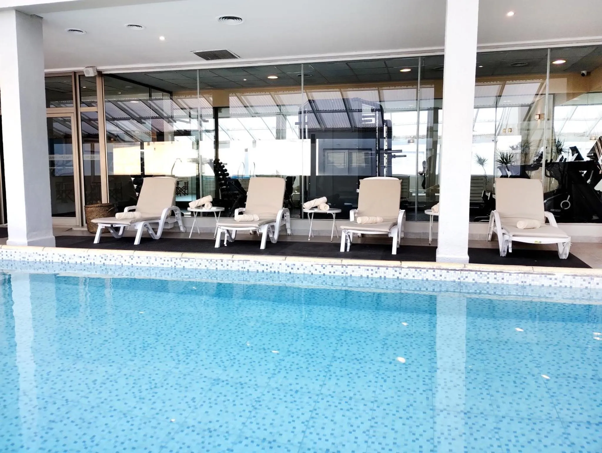 Transats alignés au bord d'une piscine intérieure lumineuse.